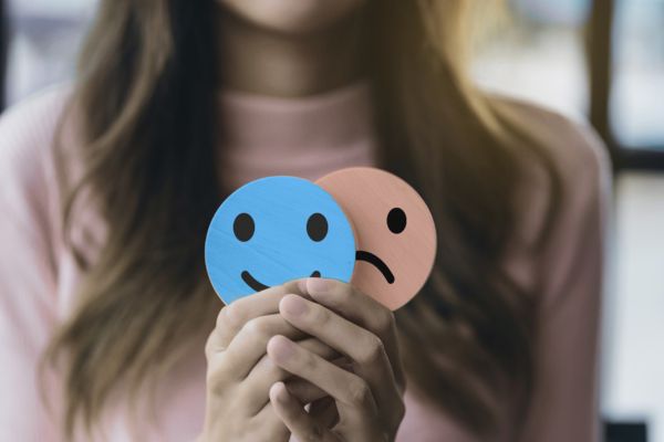 Hands holding a happy face with a sad face behind it