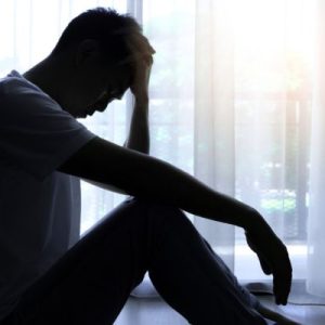 A person sitting in the corner of the room with their head on their hands in distress